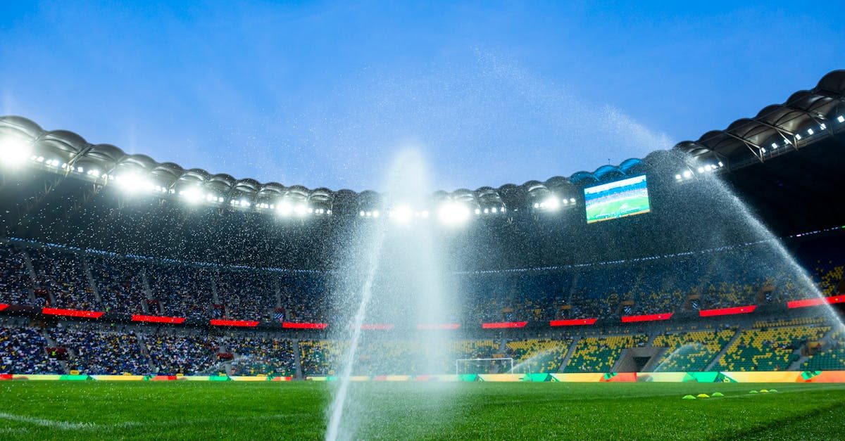 Rotor sprinklers throwing long arcs of water across a stadium field at night
