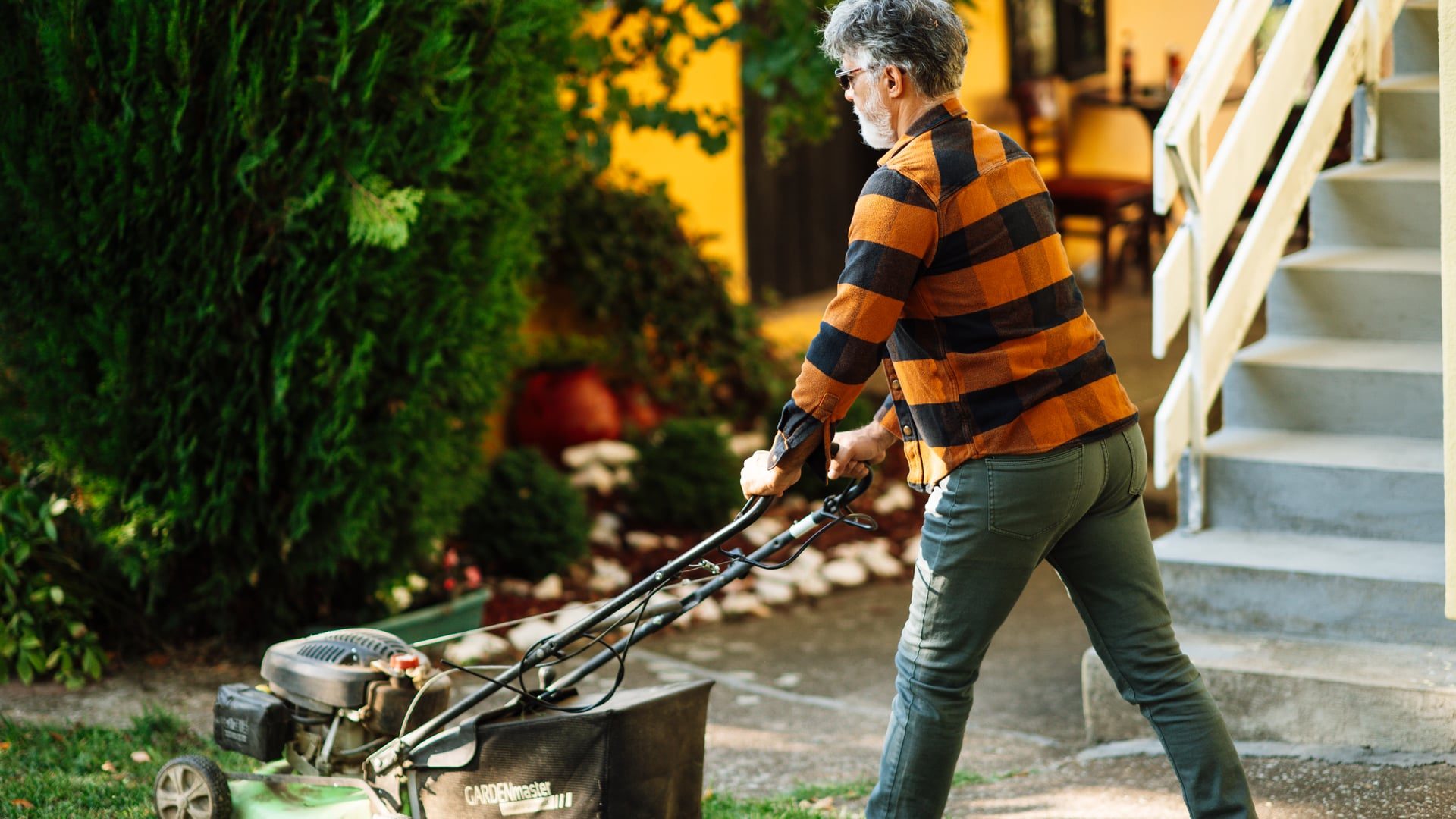Person pushing a walk-behind mower along a garden path beside a trimmed lawn