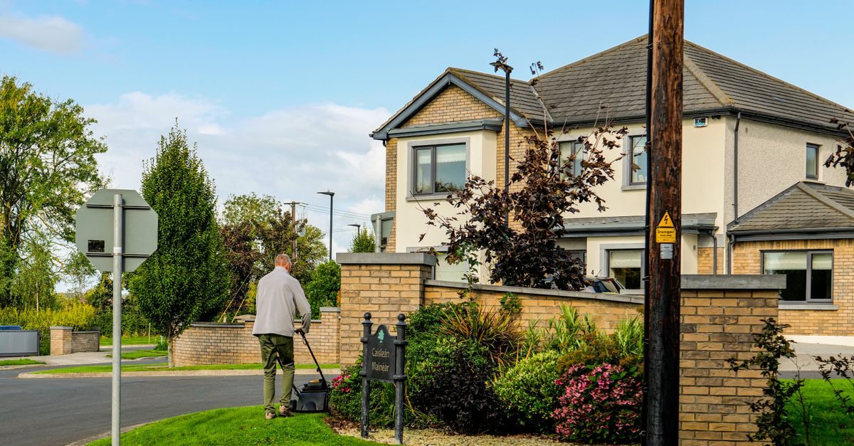 Person pushing a walk-behind mower across grass beside a house