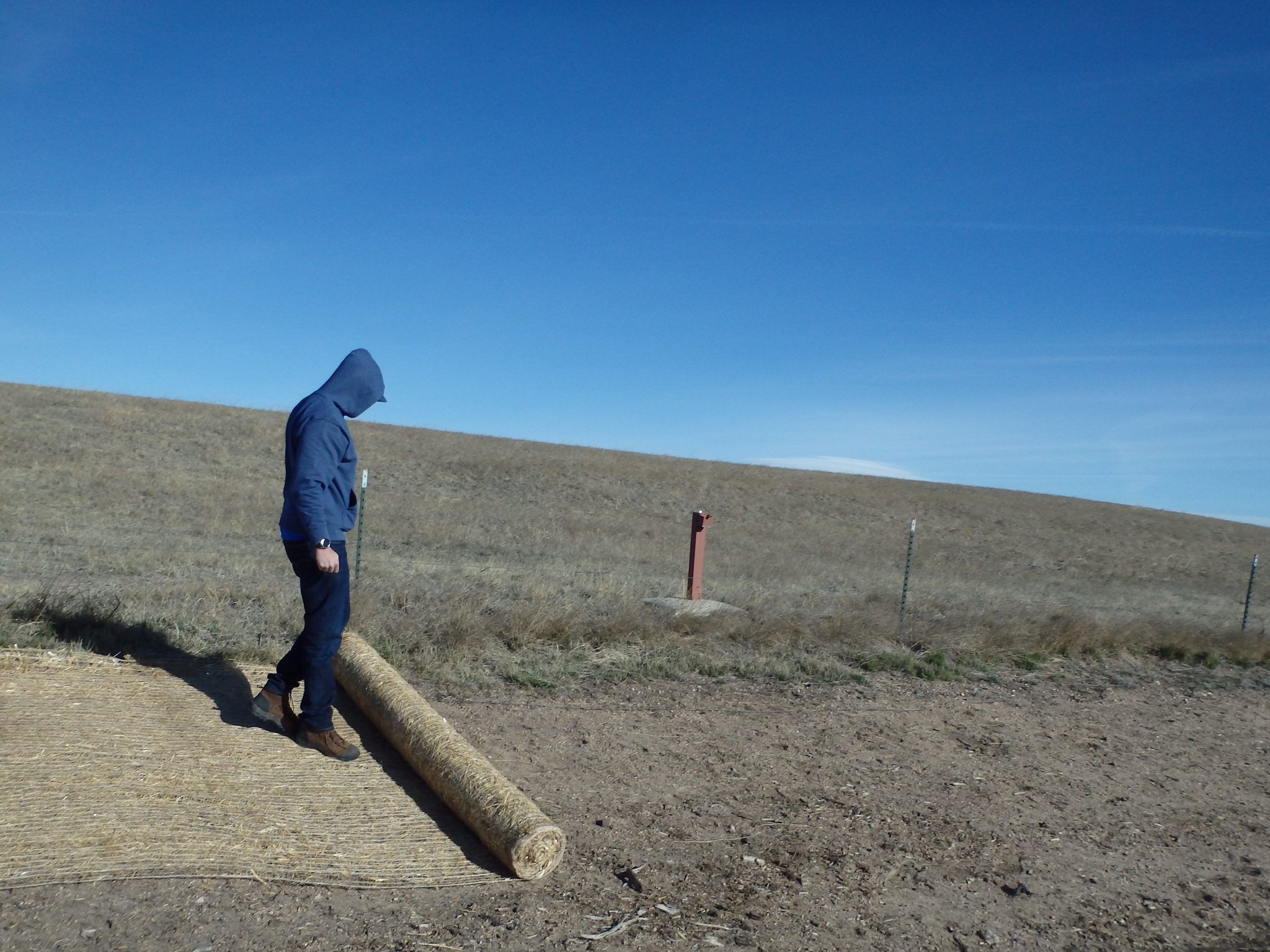Photo by Alex Schubert / USFWS on Wikimedia Commons (Public domain) Person standing beside a rolled fiber erosion-control blanket on a bare slope